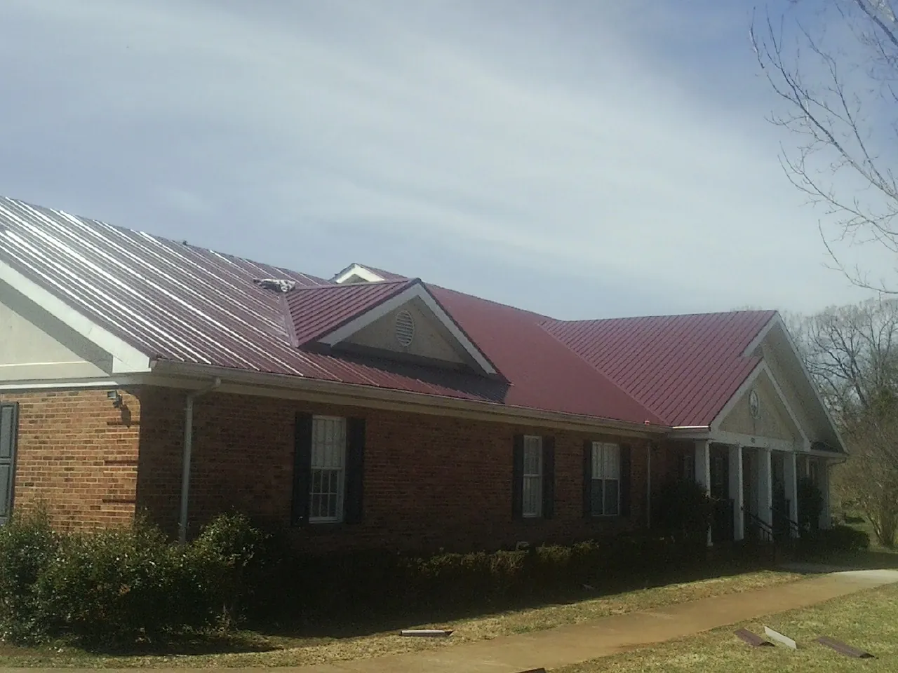 Red metal roof with gabled entries on a long brick building, from a Hail Damage Roof Repair job in Haverstraw