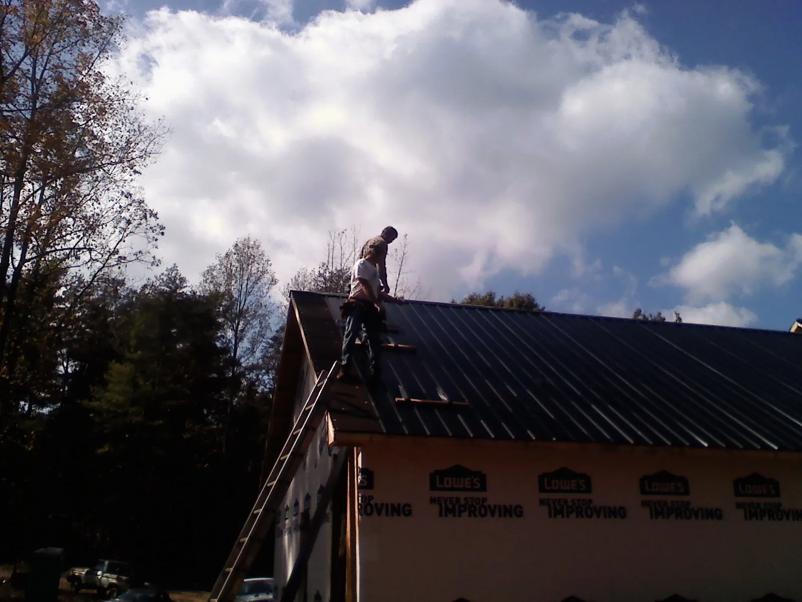Roofer fastening dark metal panels high against a cloudy sky, from a Roof Inspection job in Haverstraw