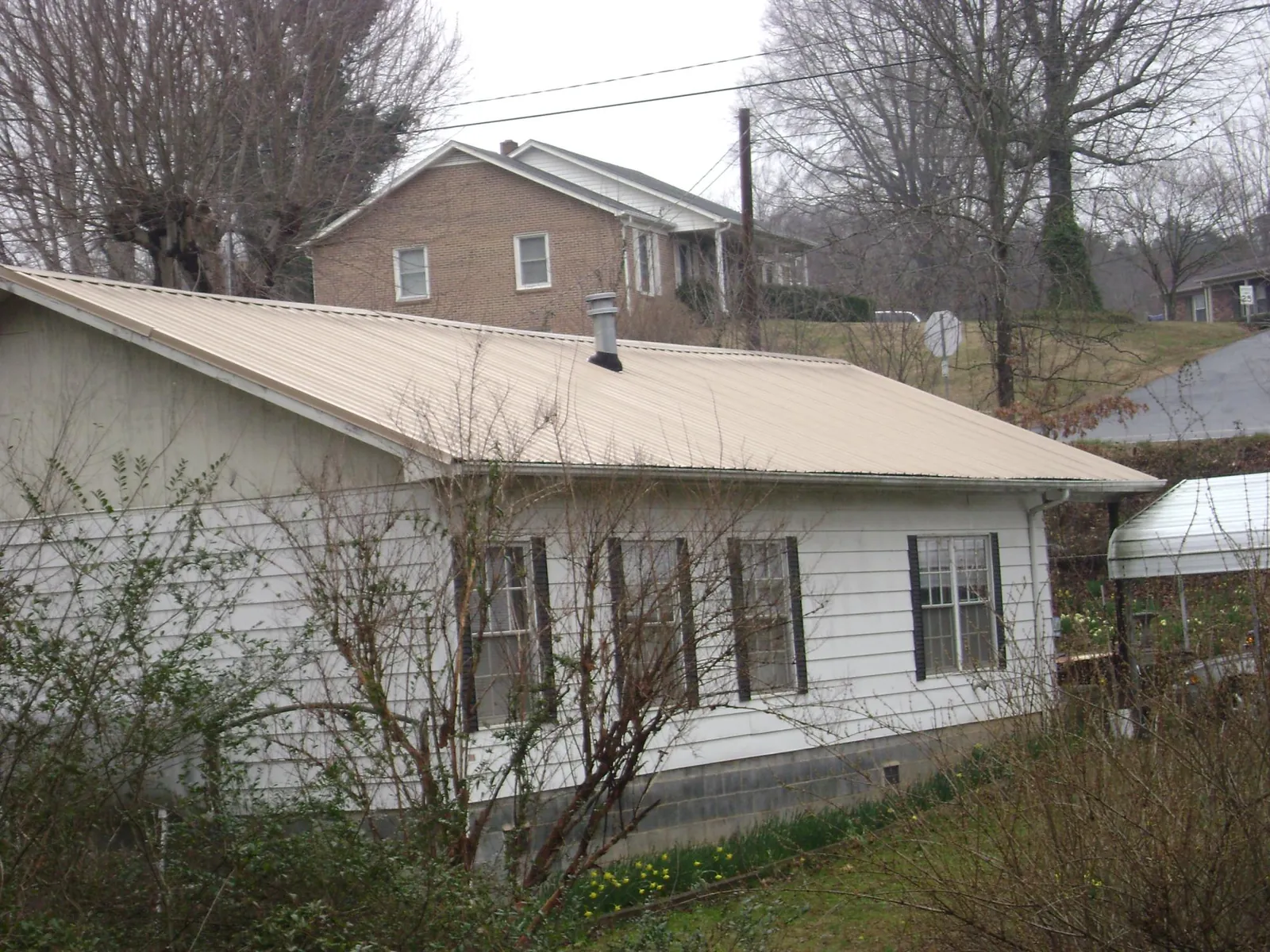 Tan metal roof on a white sided house set into a hillside — Commercial Roofing by Roofing Brothers in Haverstraw